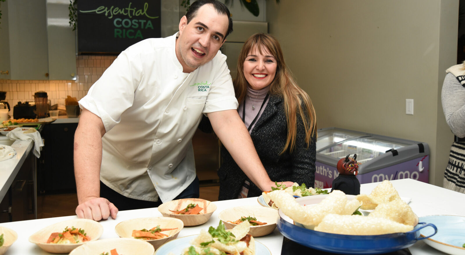 Two staff preparing and serving tacos at a food station during an event, smiling at the camera.