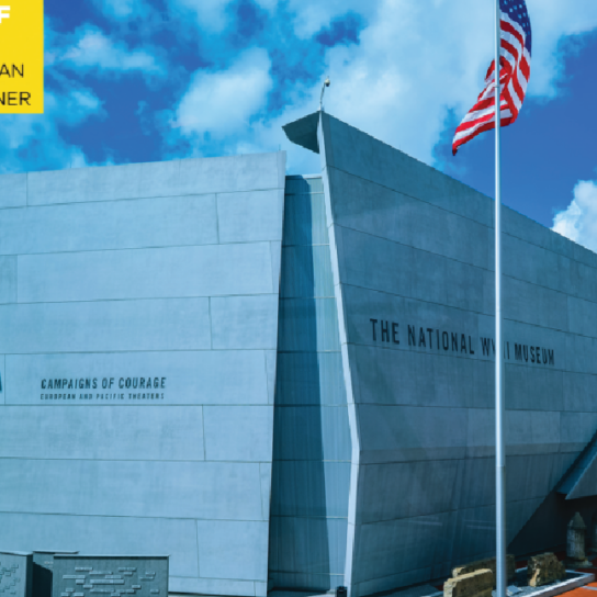 Exterior view of The National WWII Museum in New Orleans, showcasing the modern architecture of the 'Campaigns of Courage' pavilion under a clear blue sky, with the American flag proudly displayed.